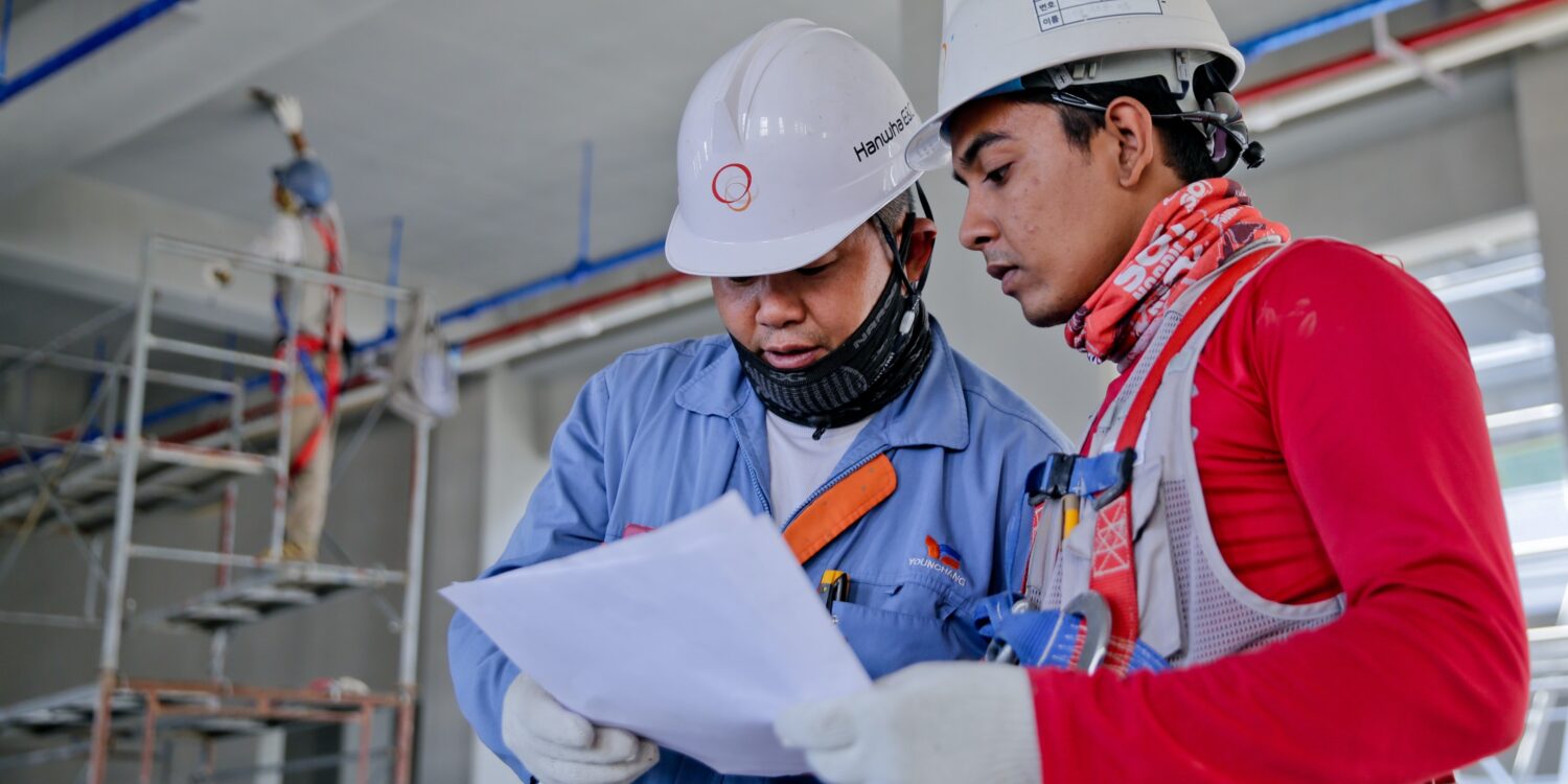 Two people look over a document on a construction site.