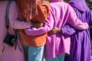 The back of four women in purple sweaters linking arms.